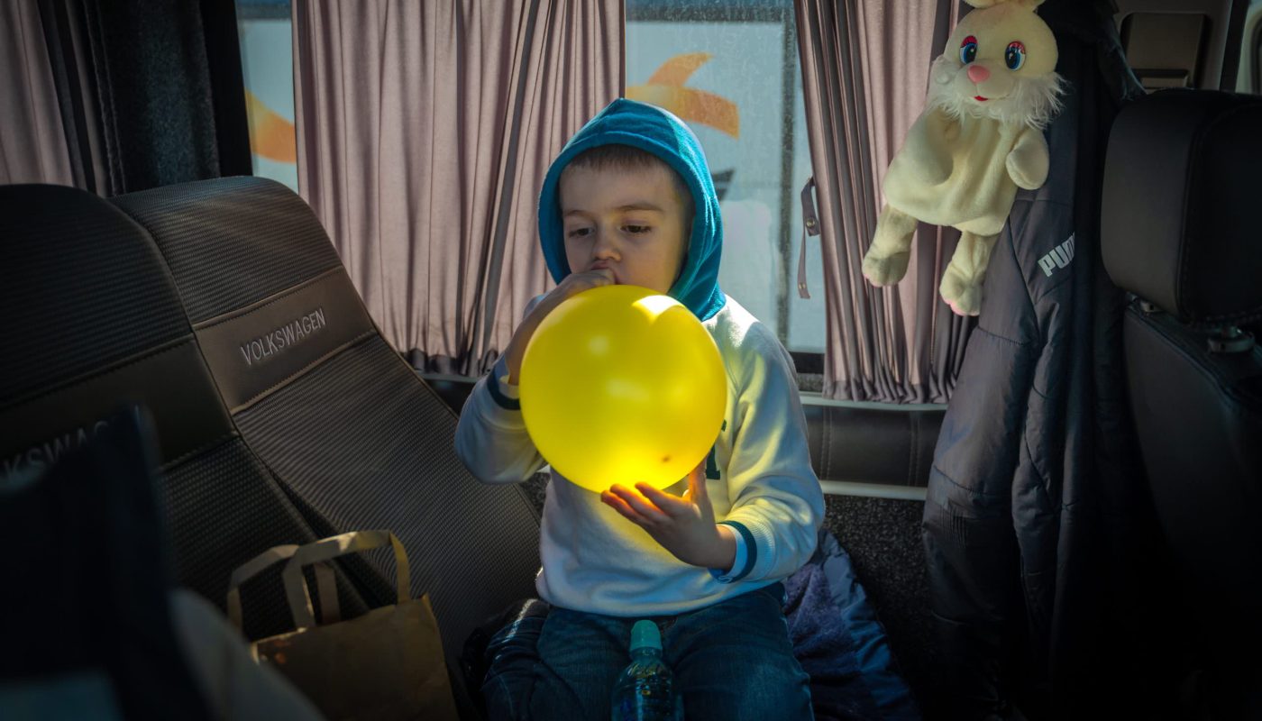 Refugees from Ukraine stop at the border as they cross from Slovenia into Italy. A young refugee plays with a balloon inside the minibus his family travelled in. ; An estimated 11,000 refugees from Ukraine have arrived in Italy since 5 March, mostly in buses, vans and private cars. Refugees have told UNHCR they are travelling to Italy to join family members or friends already in the country.